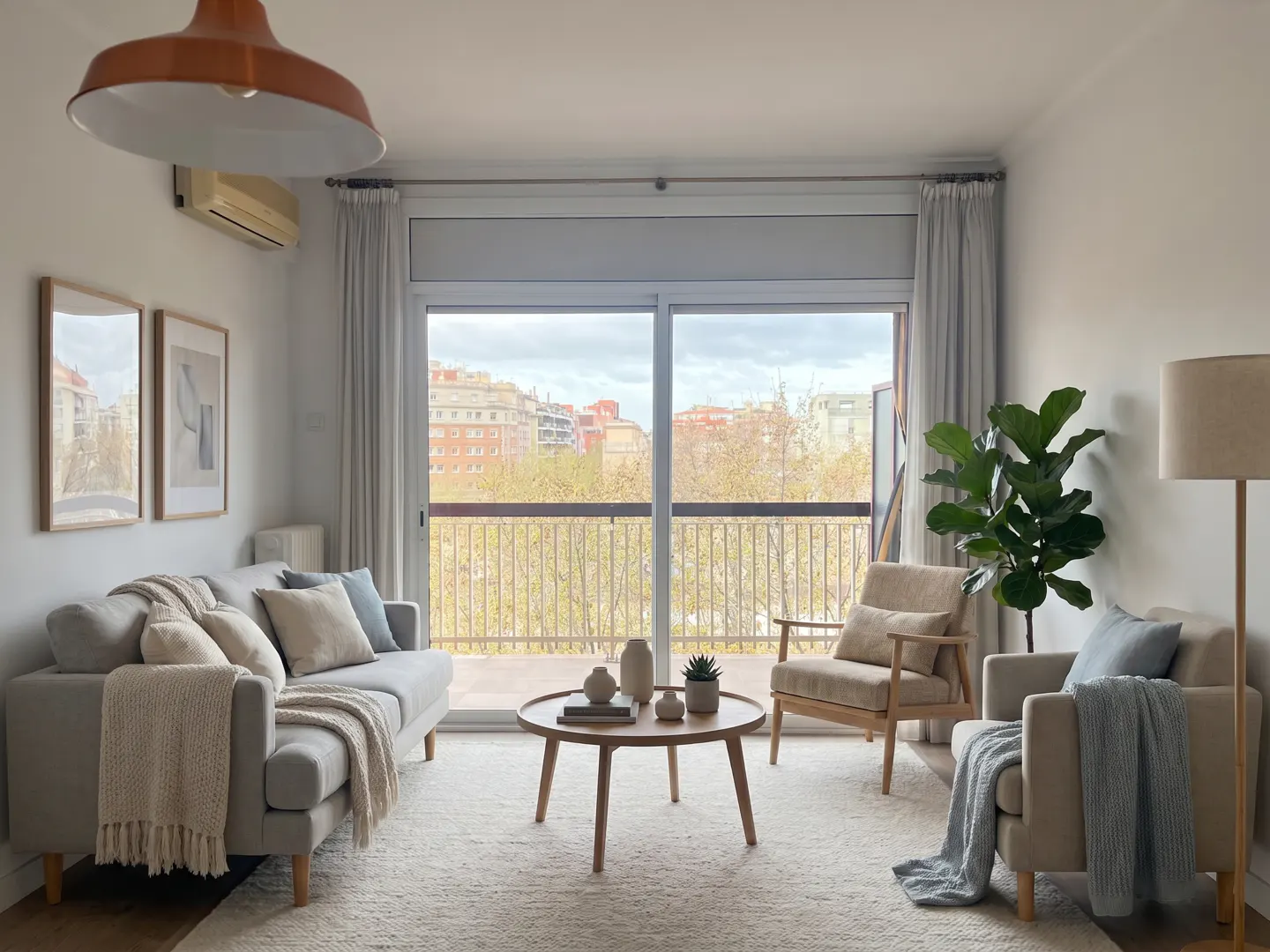 Bright living room with a grey sofa, two armchairs, a round wooden coffee table, and a balcony view of city buildings.