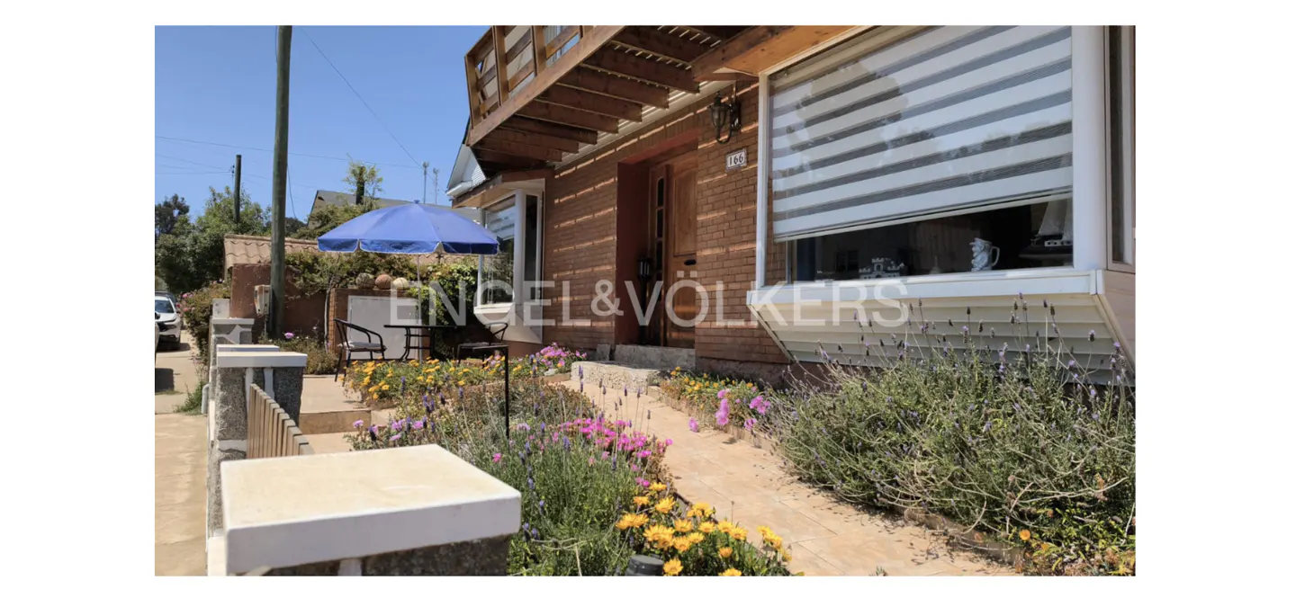 Exterior view of a brick house with a blue umbrella, flowers, and an Engel & Völkers sign.