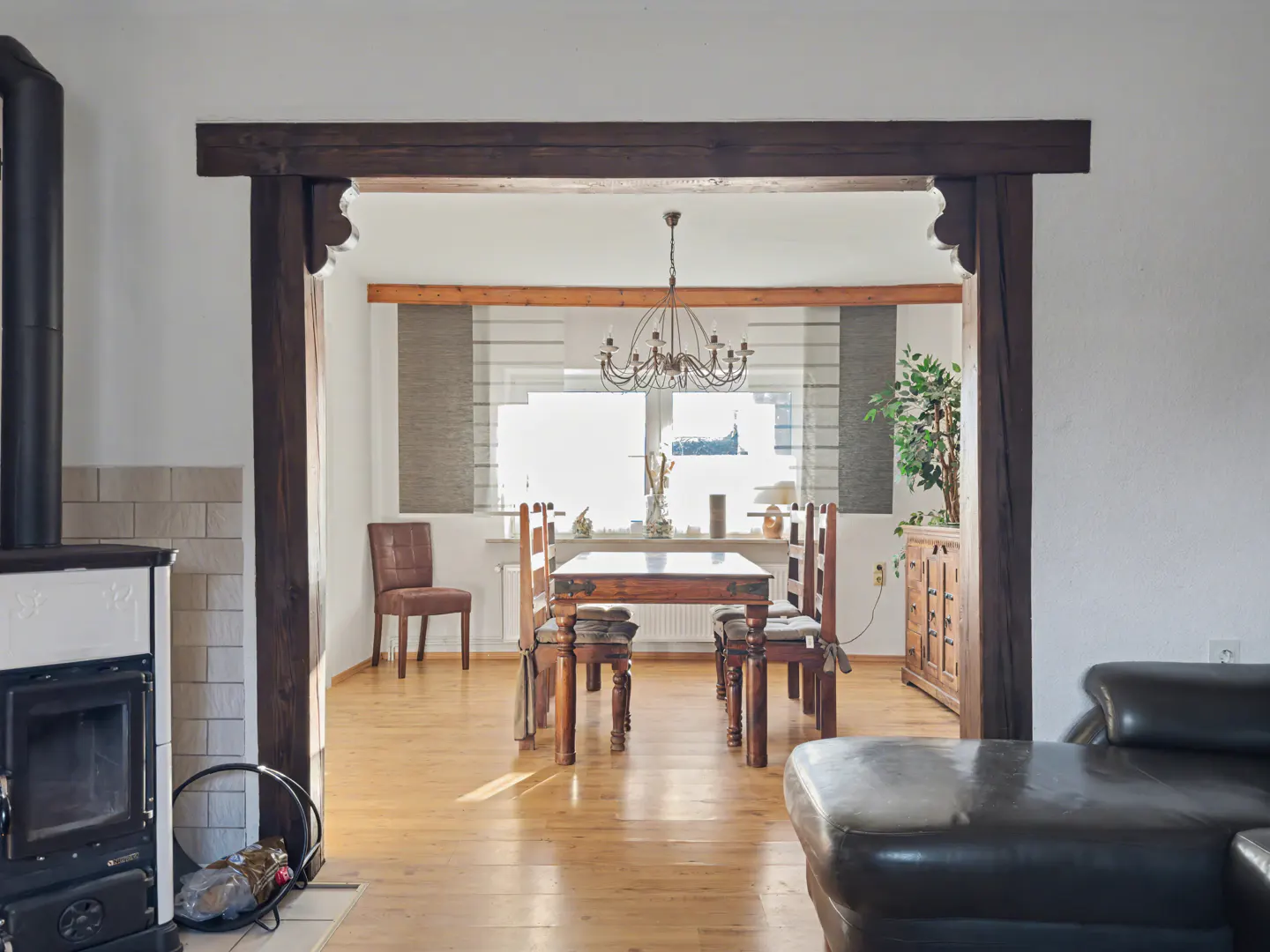 Living room view into dining room with wood table, chairs, and chandelier. A black leather couch is in the foreground.