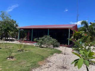 Red house with a screened-in porch, surrounded by green grass, trees, and white gravel under a blue sky.