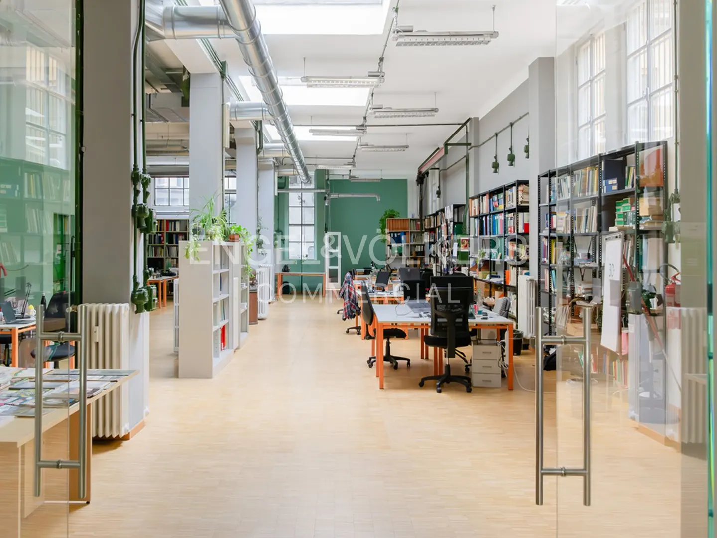 Bright, open office space with desks, bookshelves, and large windows. Light wood floors and gray walls create a modern, airy feel.