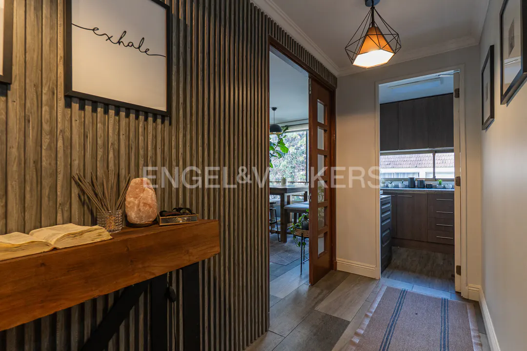 Hallway with wood-slat wall, "exhale" art, wooden console table, and view into a kitchen and dining area.