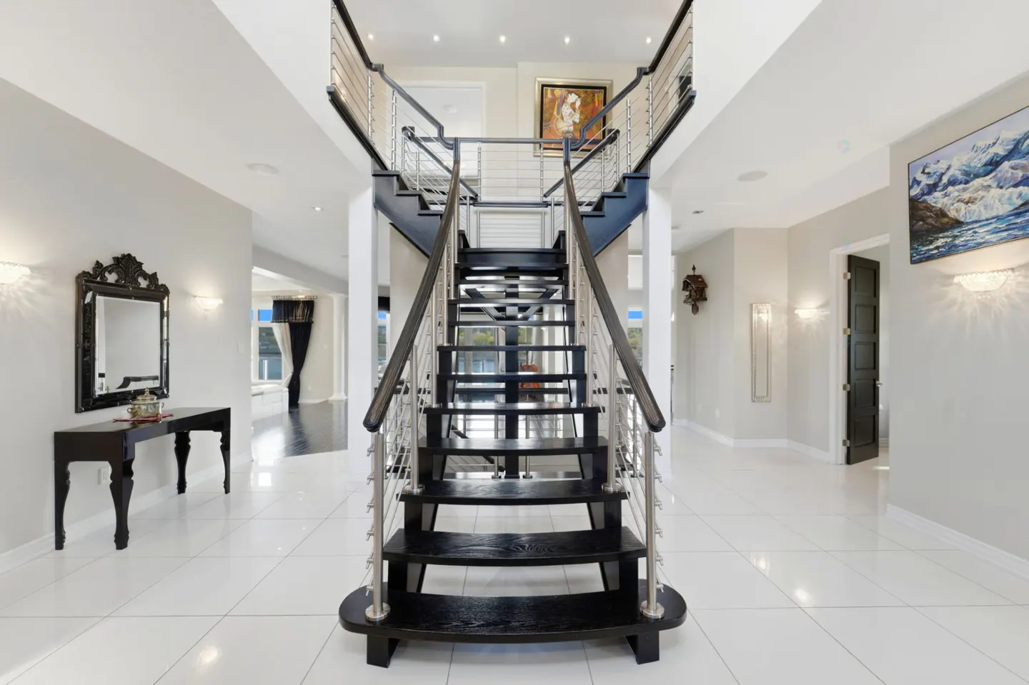 Grand foyer with white tile floors, a central black staircase with metal railings, and elegant wall decor.