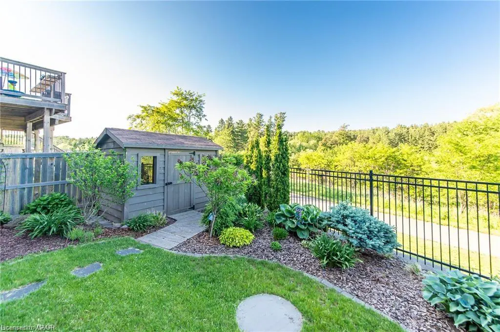 A backyard view with a gray shed, green lawn, and black metal fence against a wooded backdrop.