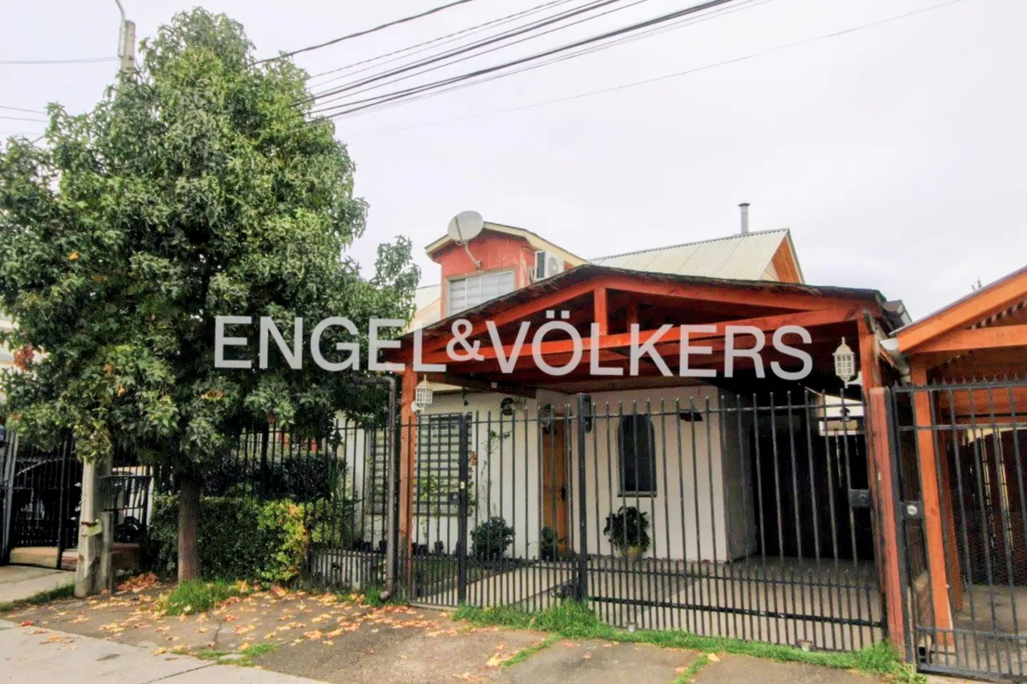 Exterior of a white house with a red roof and a black iron fence. A large tree is on the left. Engel & Völkers logo is superimposed.