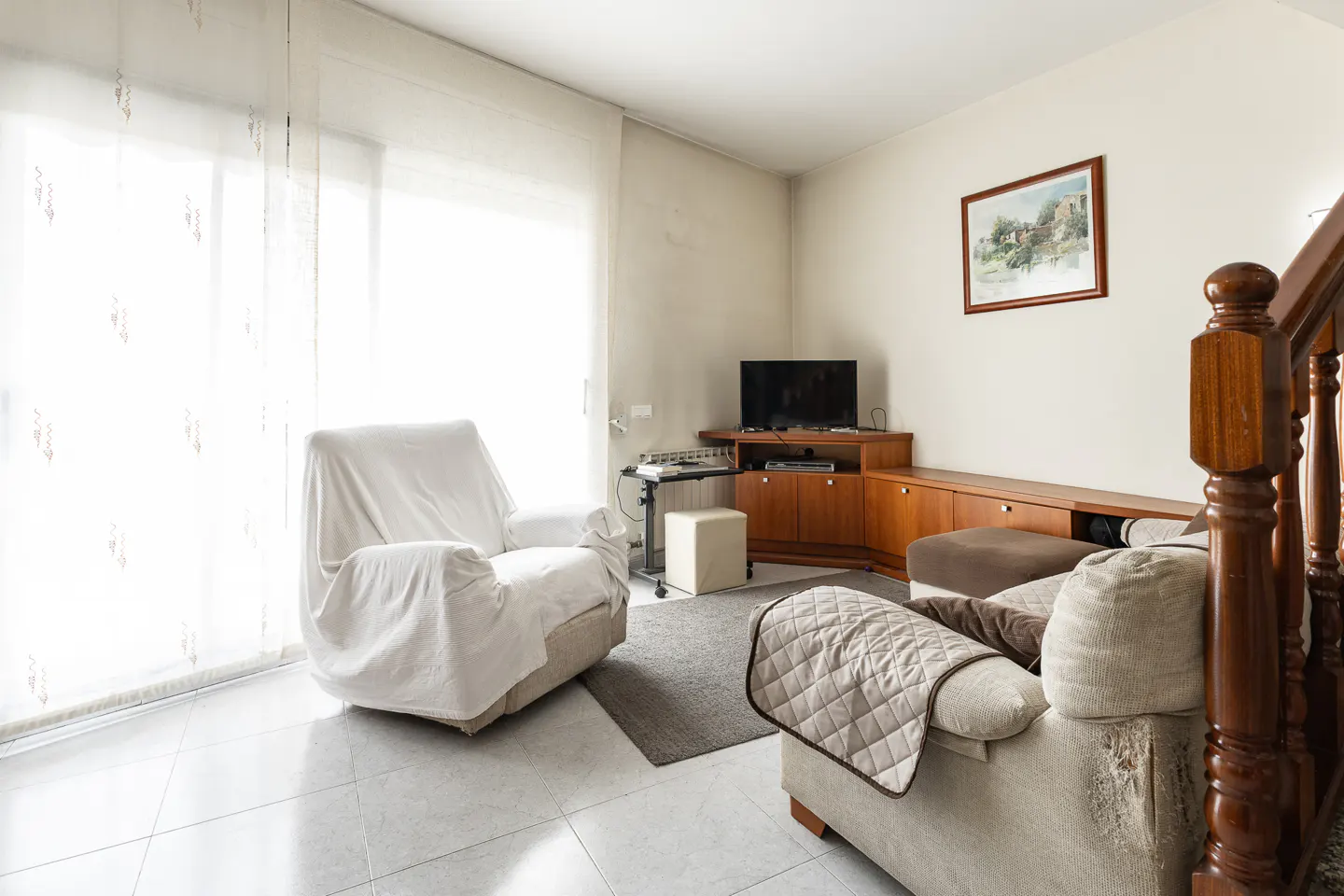Living room with a covered armchair, a sofa with a quilt, a TV, and a painting on the wall.