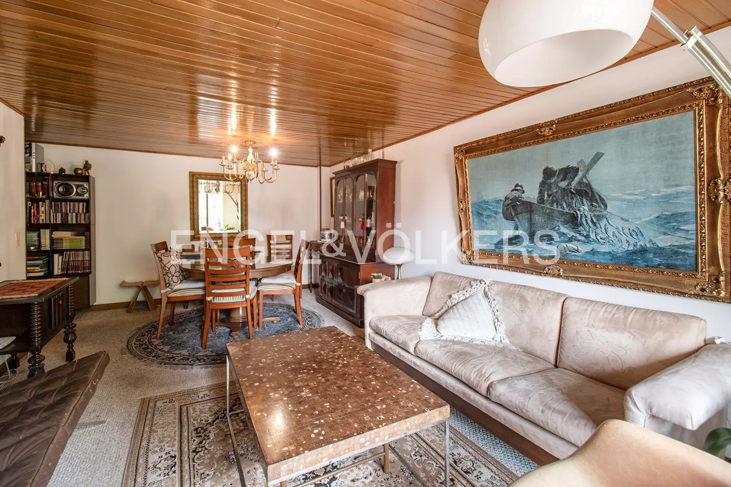 A living and dining area with a beige sofa, wooden table, and a painting in a gold frame.