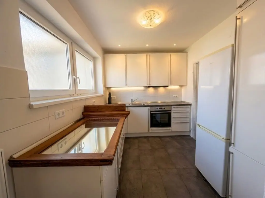 Bright kitchen with white cabinets, stainless steel appliances, and a wooden countertop. A large window provides natural light.