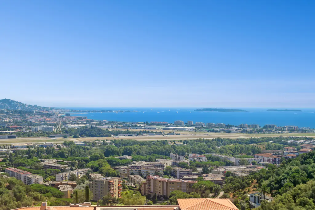 Scenic view of Cannes, France, featuring buildings, trees, and the Mediterranean Sea under a clear blue sky.
