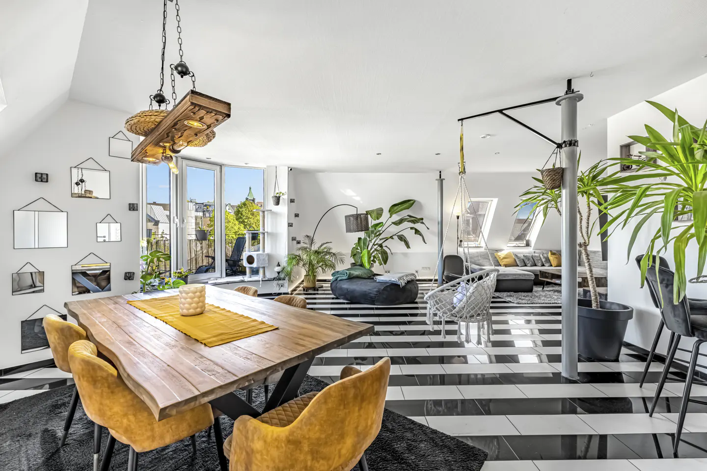 Open-concept living space with black and white striped floors, a wooden dining table with yellow chairs, and many plants.