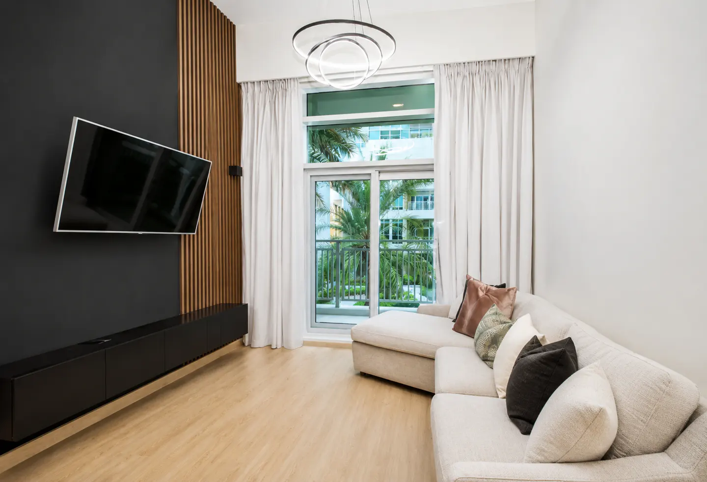 Living room with a black accent wall, TV, console, and a white sectional sofa near a window with palm tree views.
