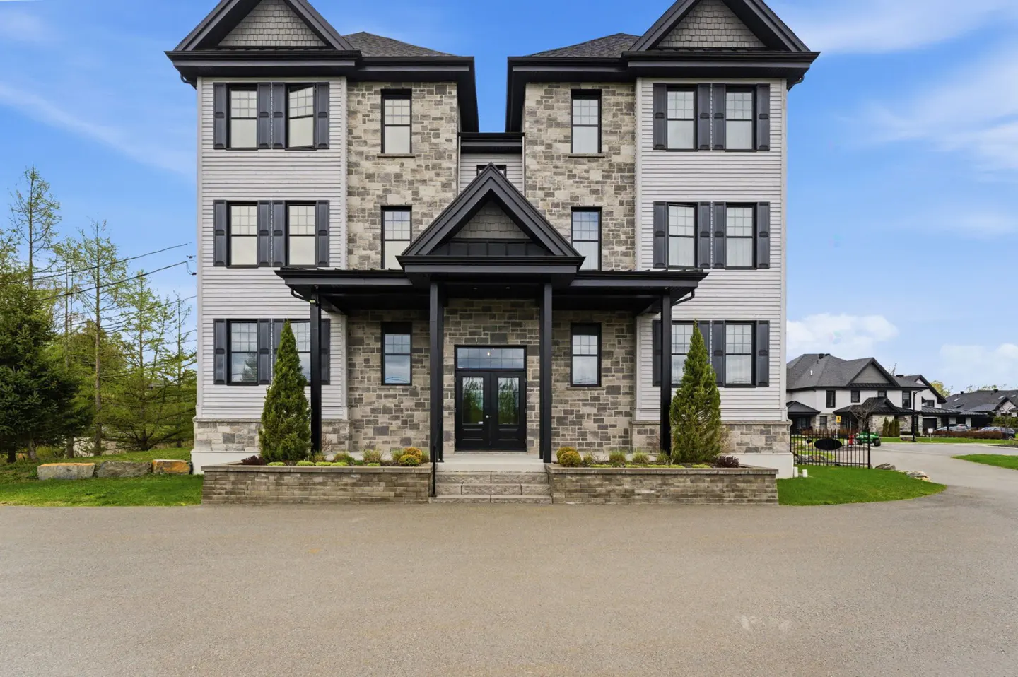 Three-story townhouse with gray stone and siding, black trim, and a covered porch with a double door entrance.