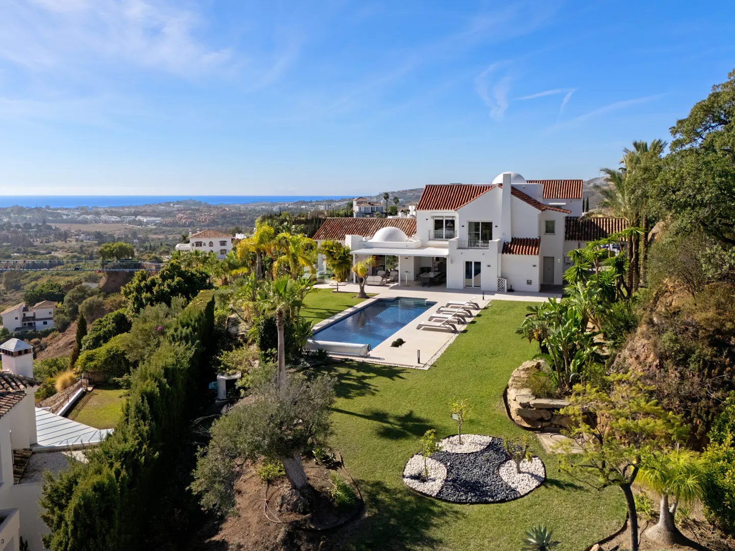Aerial view of a white villa with a red tile roof, a pool, and a green lawn on a sunny day.