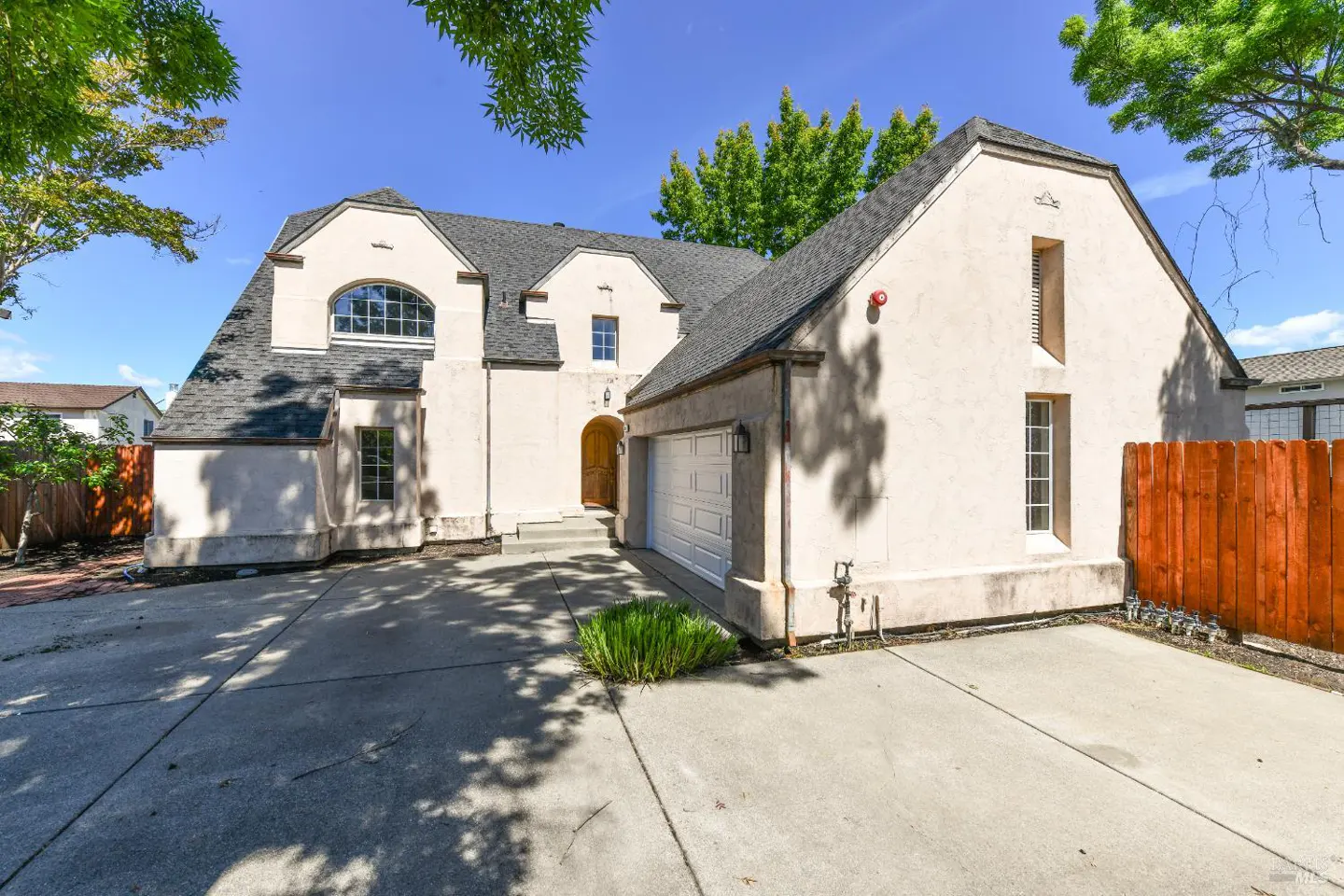 Exterior of a two-story beige house with a gray roof, white garage door, and concrete driveway on a sunny day.
