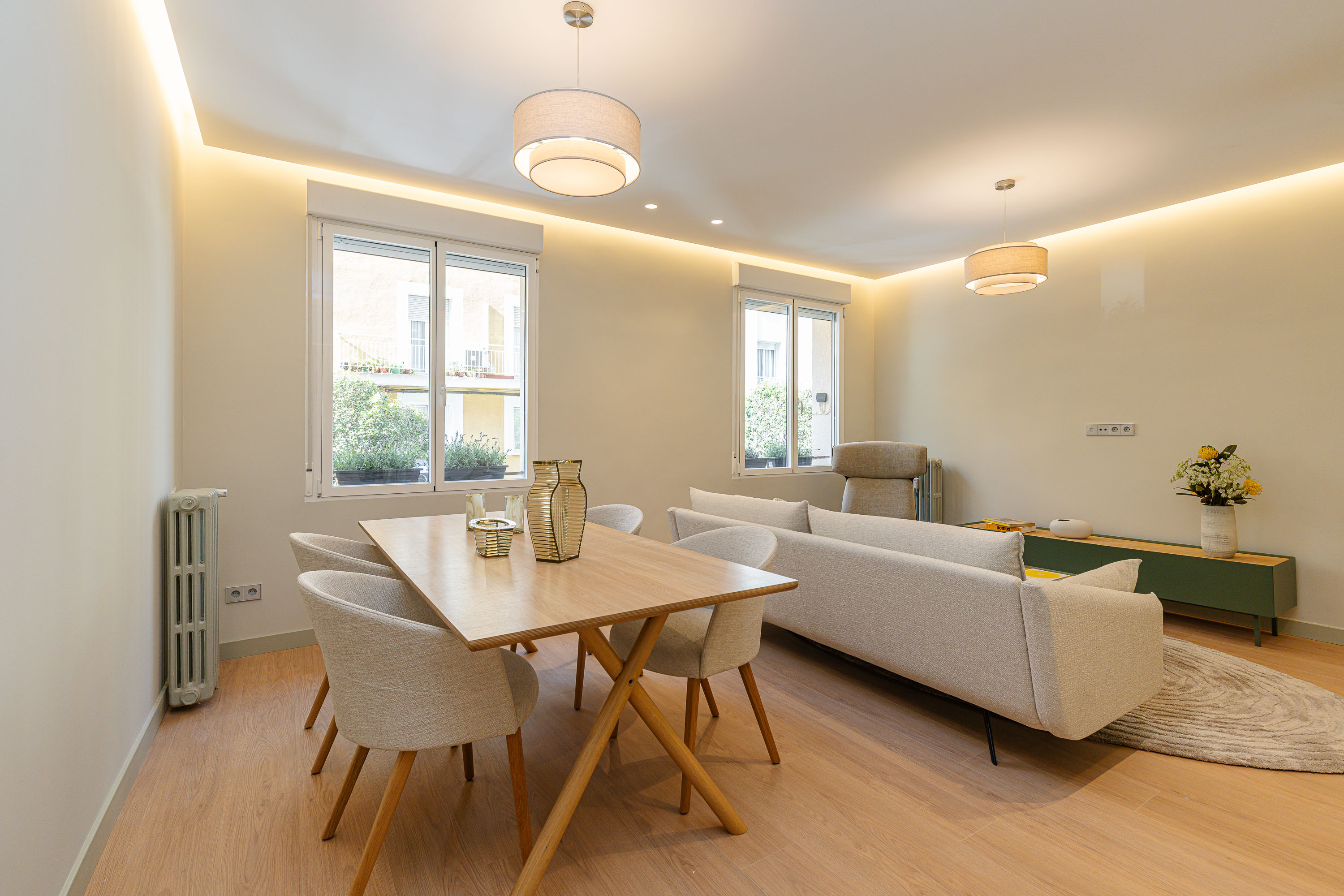 Modern living room with light wood floors, a dining table with four chairs, and a beige sofa under recessed lighting.