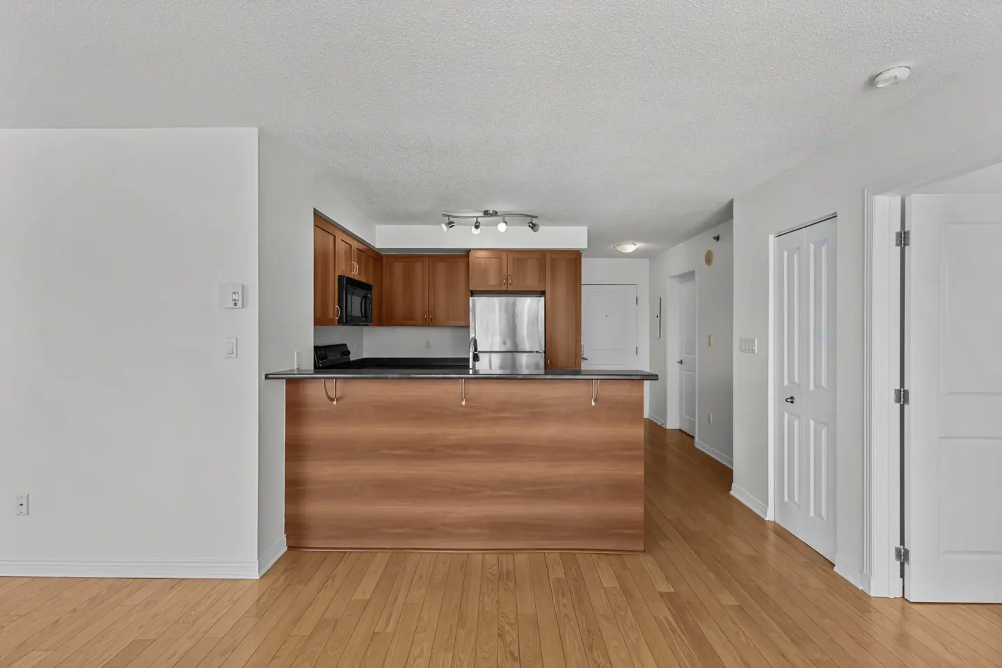 A condo interior with wood floors, white walls, and a kitchen with wood cabinets and stainless steel appliances.
