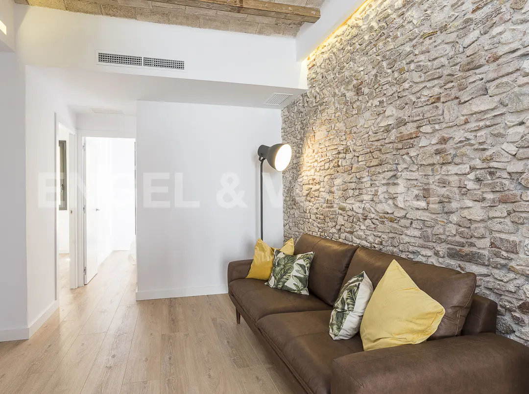 Brown leather sofa with yellow and patterned pillows against a rustic stone wall in a modern living room with wood floors.