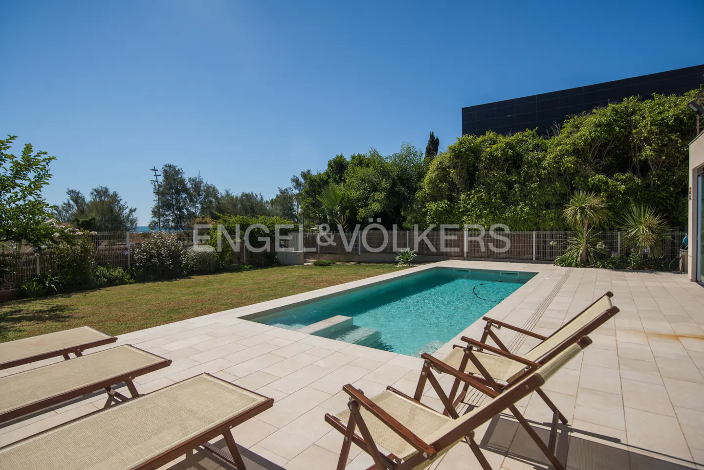 A backyard with a pool, lounge chairs, and green grass under a clear blue sky.