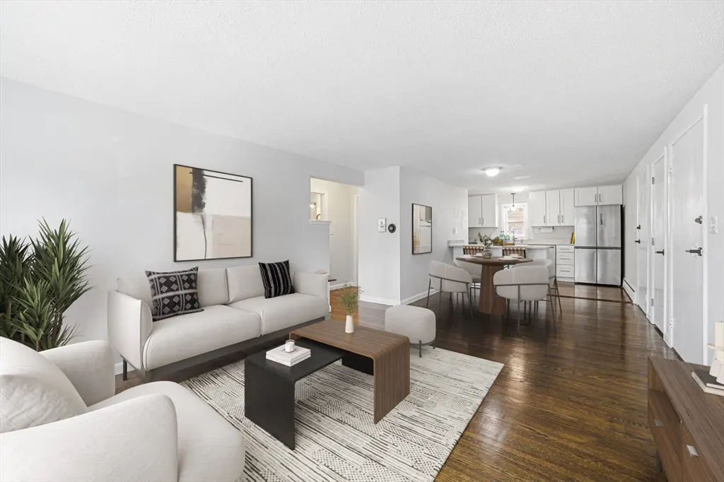 Bright, open-concept living space with white sofas, dark wood floors, and a modern kitchen in the background.