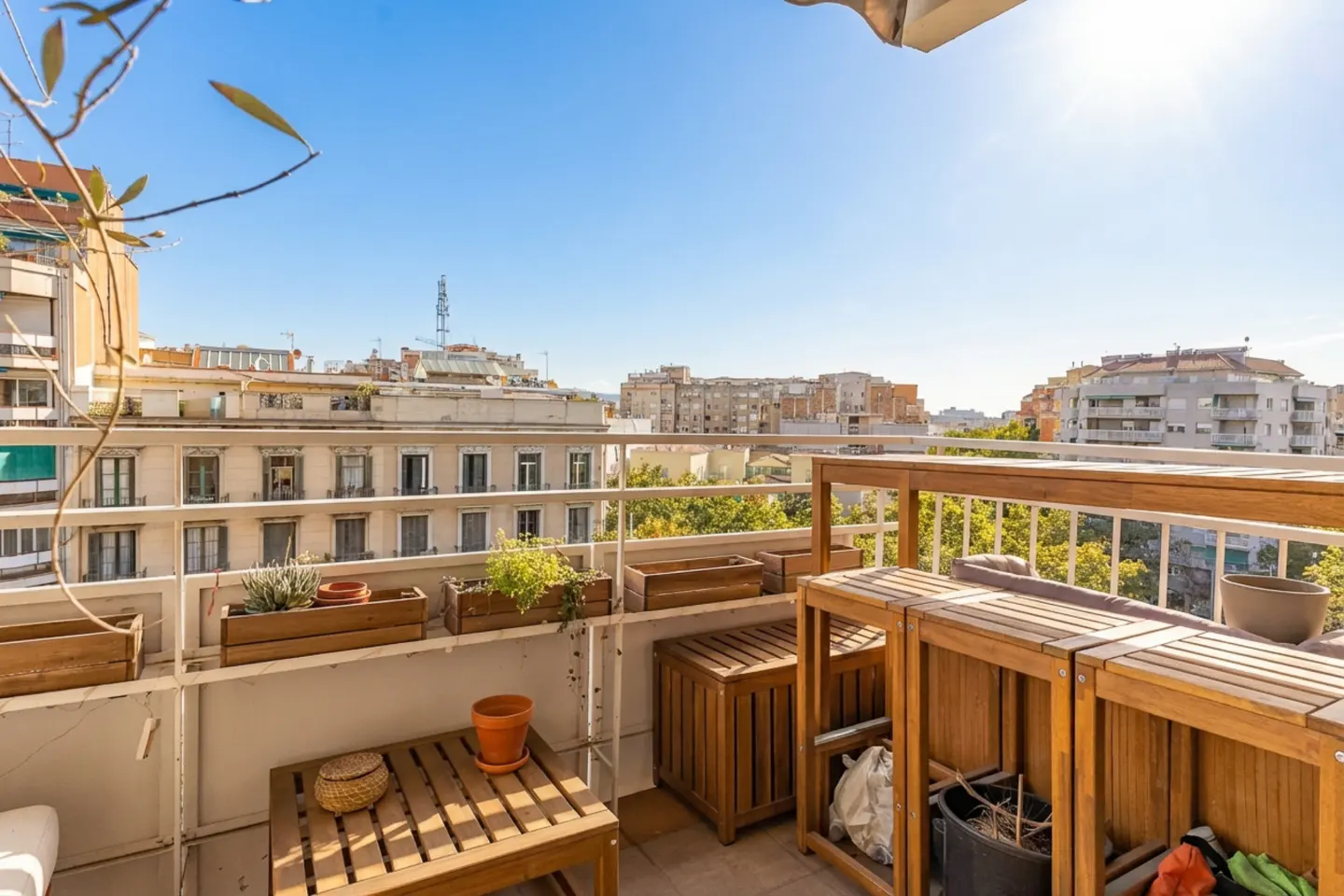 Balcony with wooden furniture, planters, and a view of city buildings under a clear blue sky.
