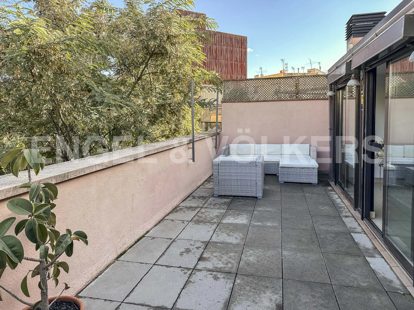 Spacious rooftop terrace with light pink walls, grey tiled floor, wicker lounge furniture, and a potted plant.