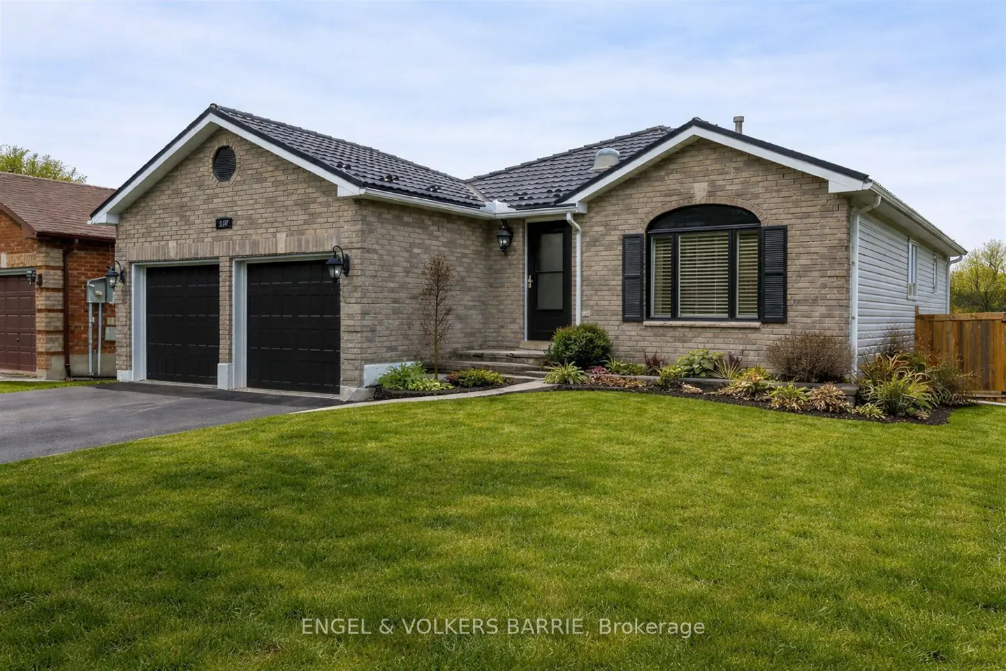 A single-story brick house with a black roof, black garage doors, and a green lawn.
