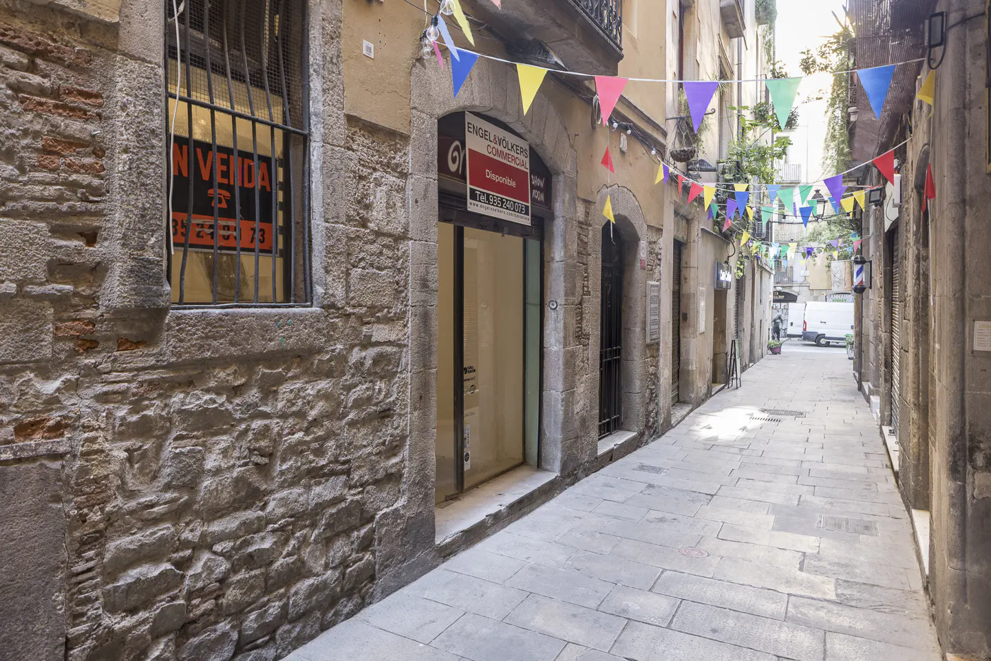 Narrow European street with stone buildings, colorful pennants overhead, and an Engel & Volkers commercial real estate office.
