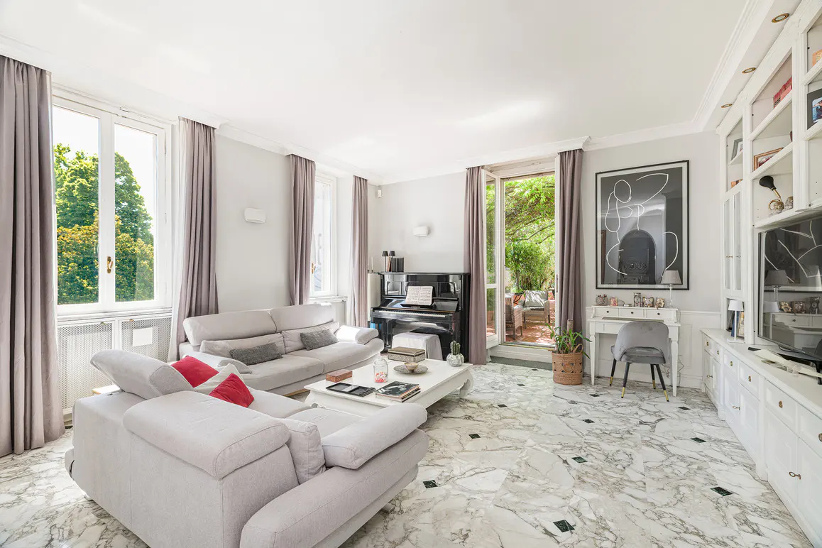 Bright living room with marble floors, gray sofas with red pillows, a black piano, and a white built-in cabinet.