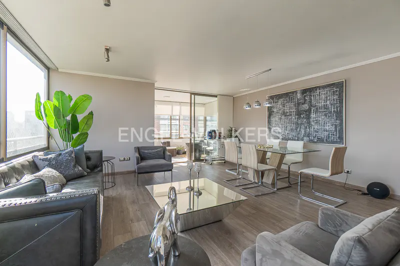 Spacious living and dining area with gray sofas, glass table, and abstract art. Light wood floors and large windows.