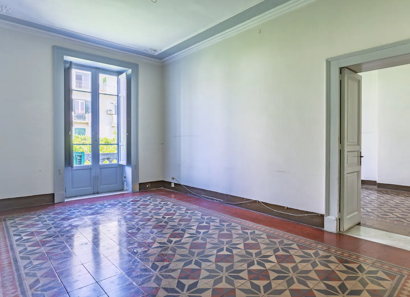 Empty room with white walls, patterned tile flooring, a blue-framed glass door to a balcony, and an open doorway.