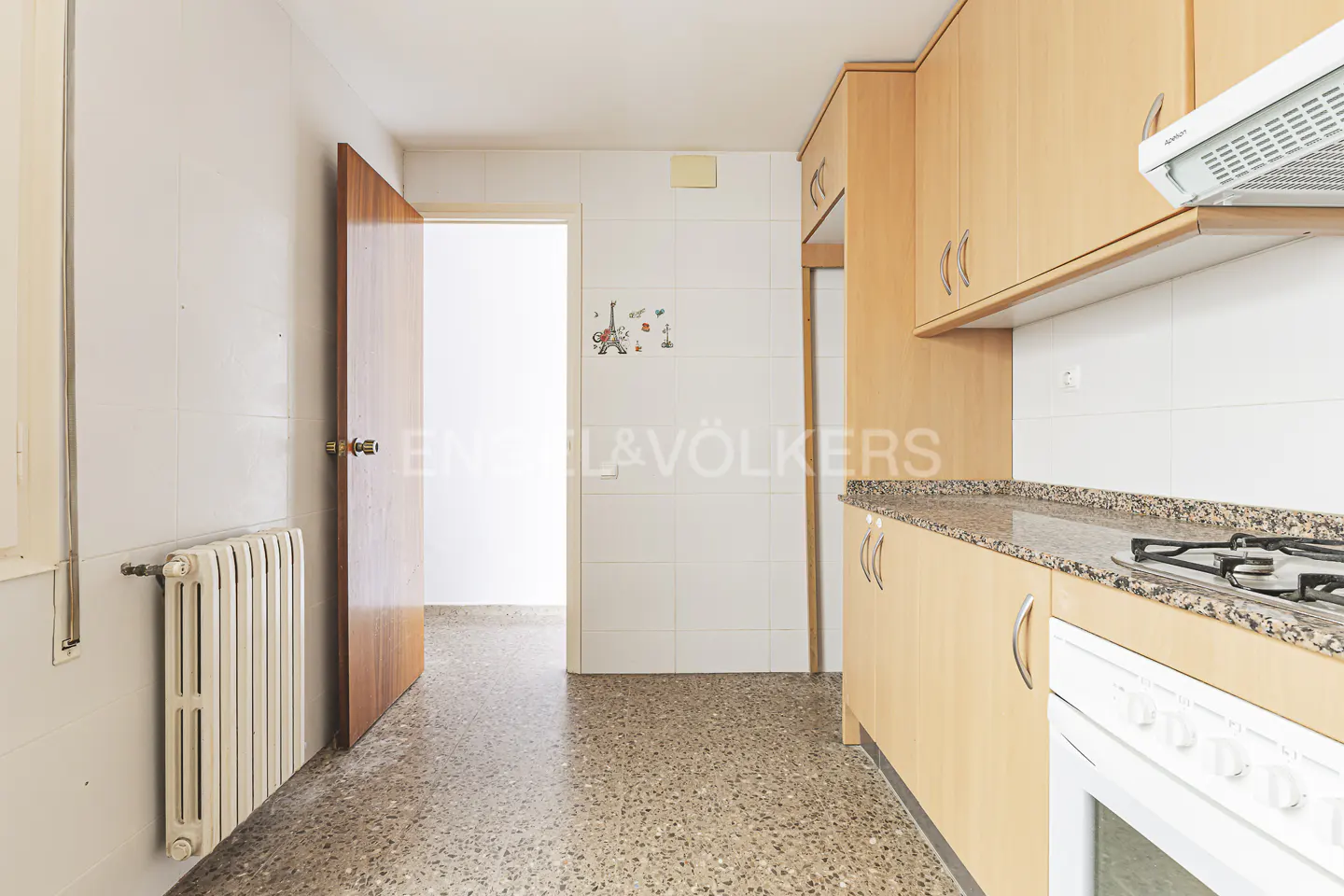 A bright kitchen with light wood cabinets, granite countertops, and a white stove. A doorway leads to another room.