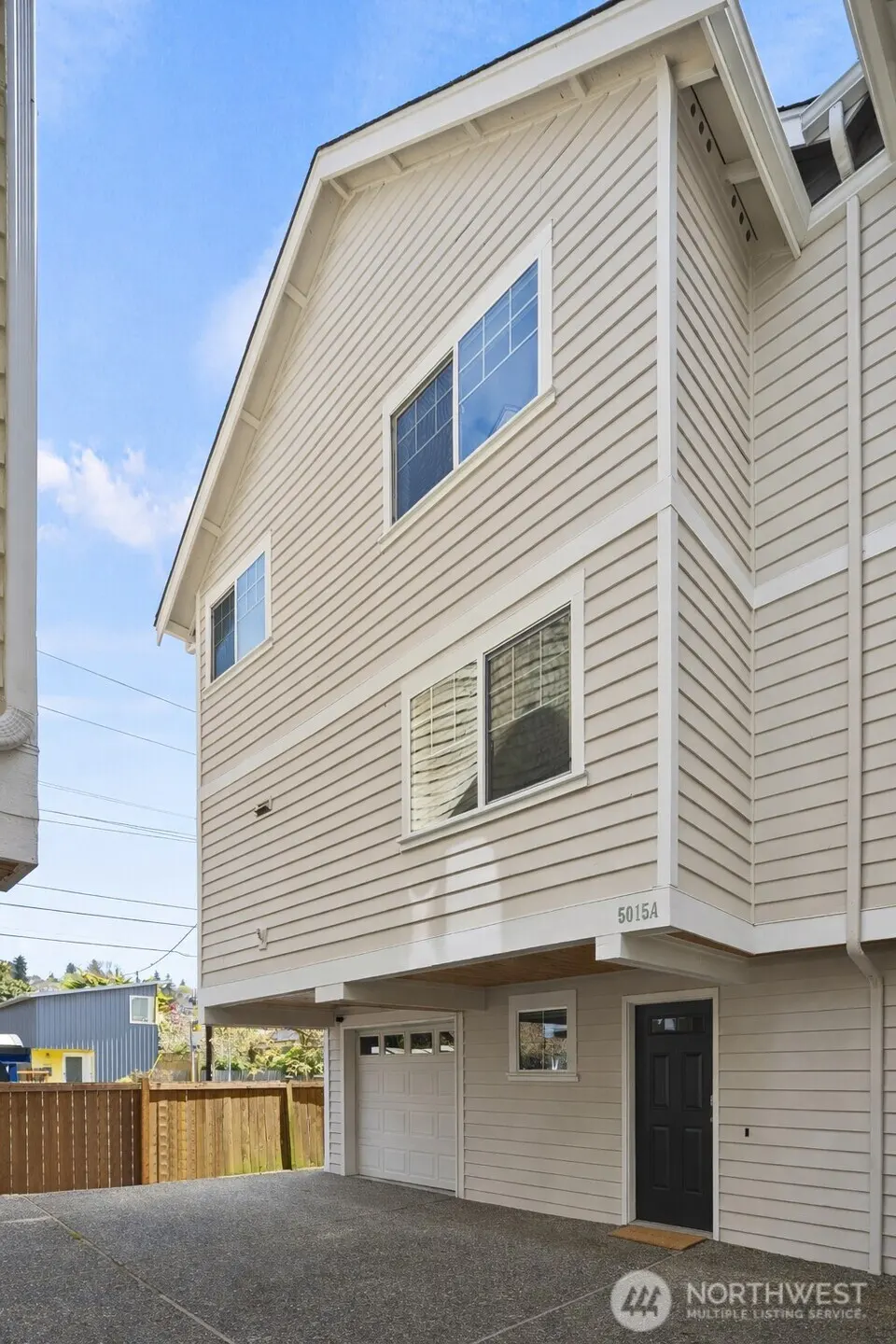 Exterior view of a two-story beige house with white trim, a black front door, and a white garage door. Windows reflect the blue sky.
