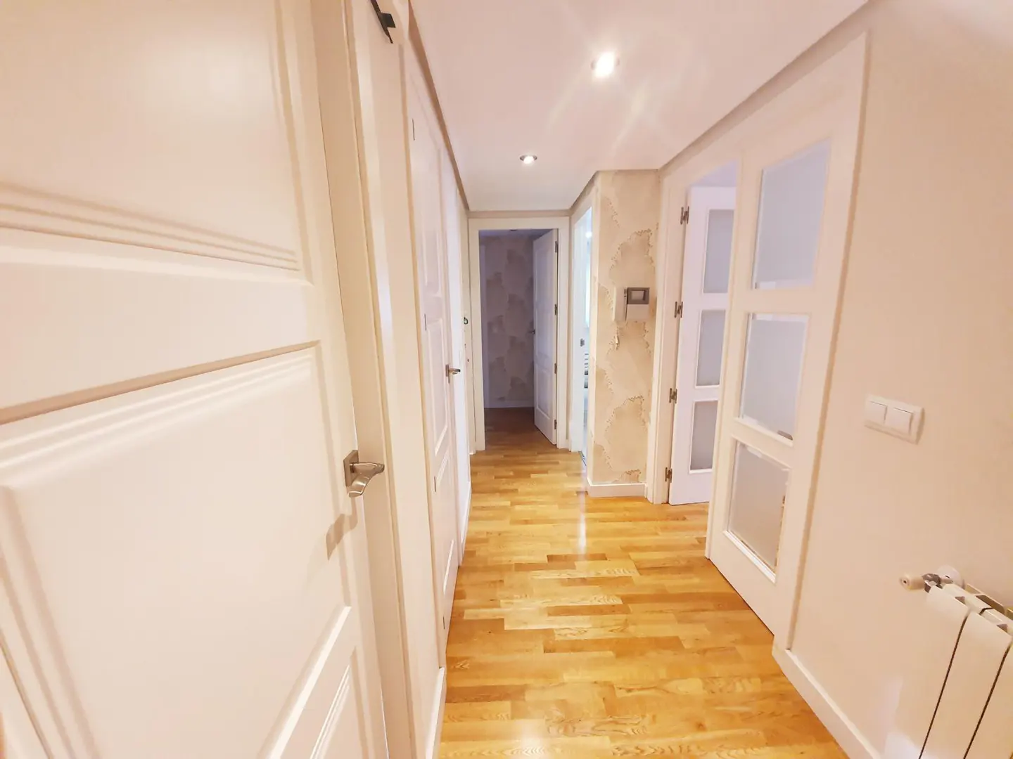 Hallway with light wood floors, white doors, and beige walls. A radiator is visible on the right.