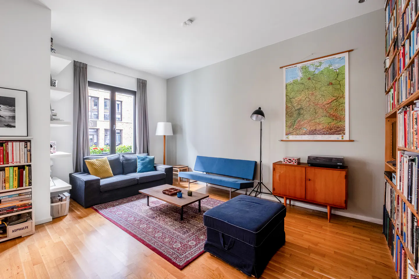 Living room with a blue sofa, matching ottoman, wooden coffee table, floor lamp, and floor-to-ceiling bookshelves.