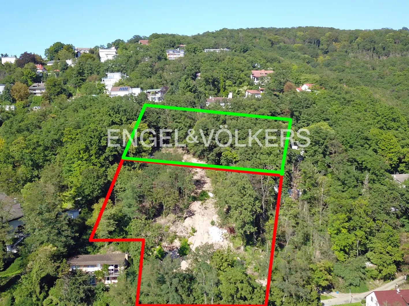 Aerial view of a wooded lot on a hillside, outlined in red and green, with the Engel & Völkers logo overlaid.