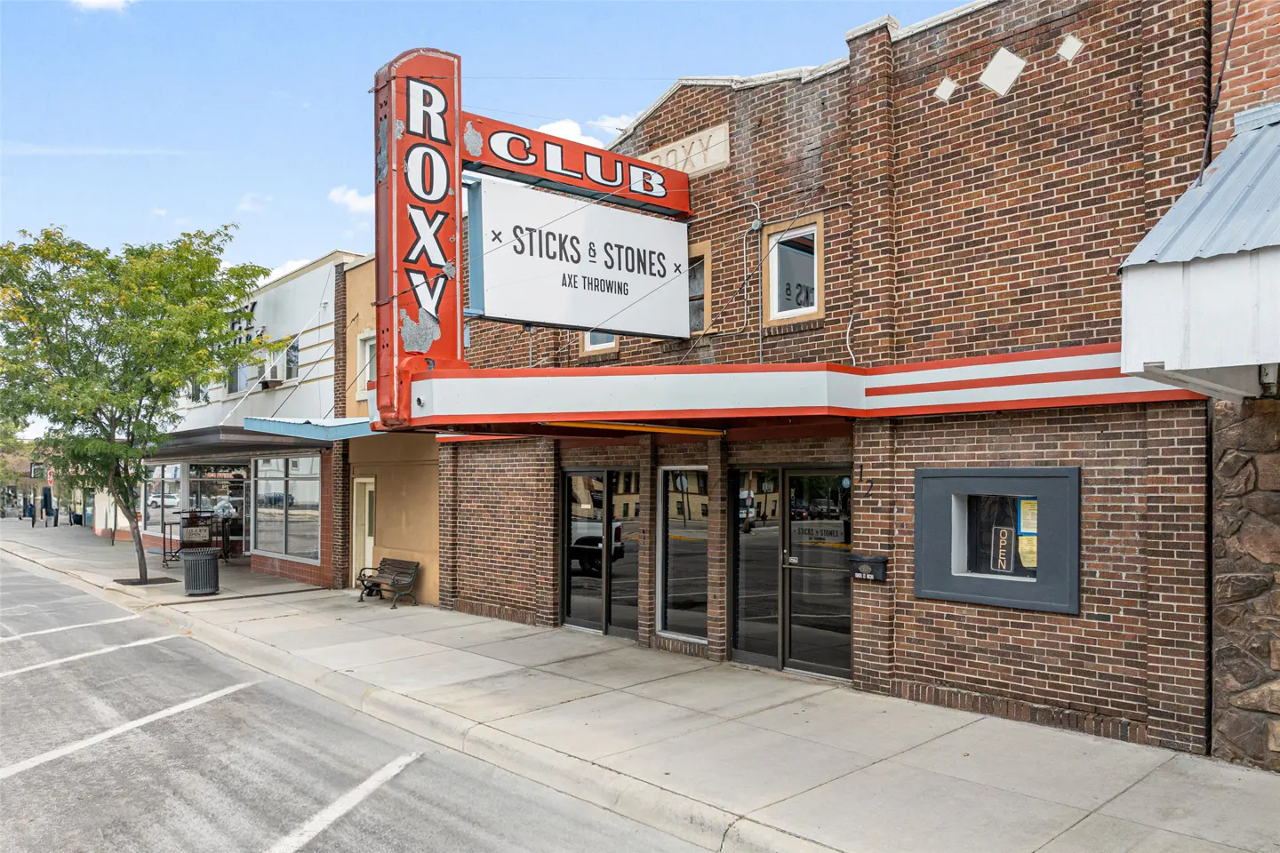 Exterior of the Roxy Club, a brick building with a red neon sign advertising "Sticks & Stones Axe Throwing."