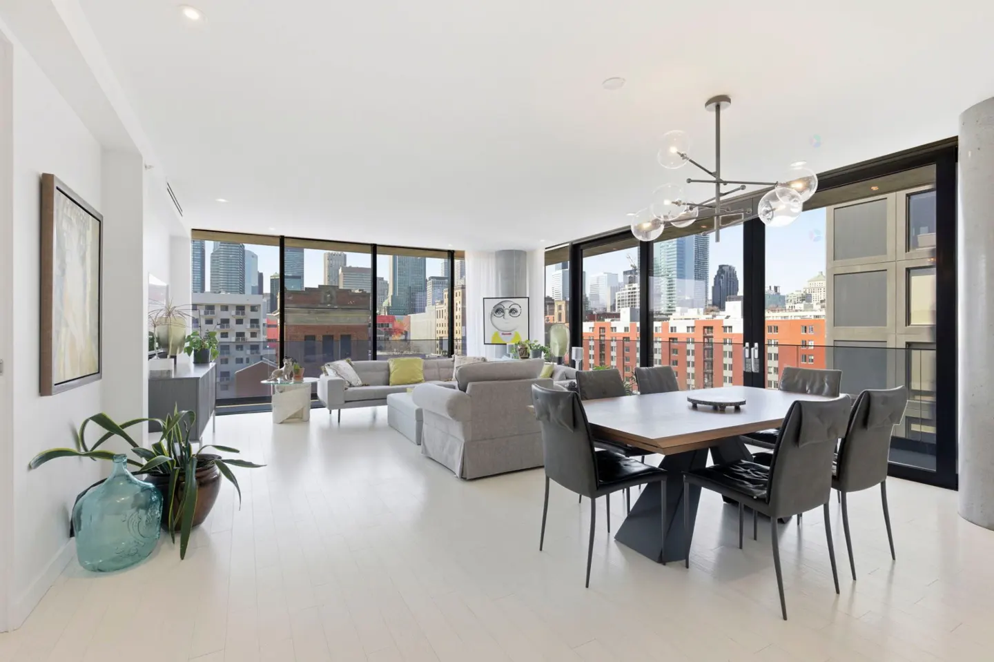 Bright, modern living and dining area with white floors, gray furniture, and a city view from large windows.