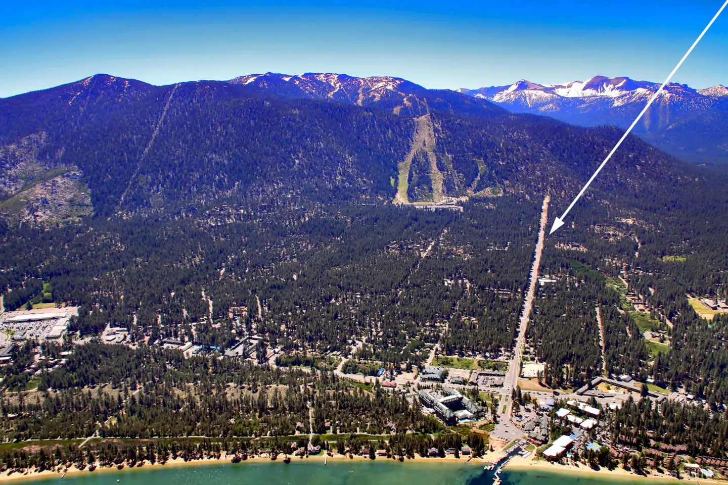 Aerial view of a town nestled between a lake and mountains, with a road leading towards a ski slope.