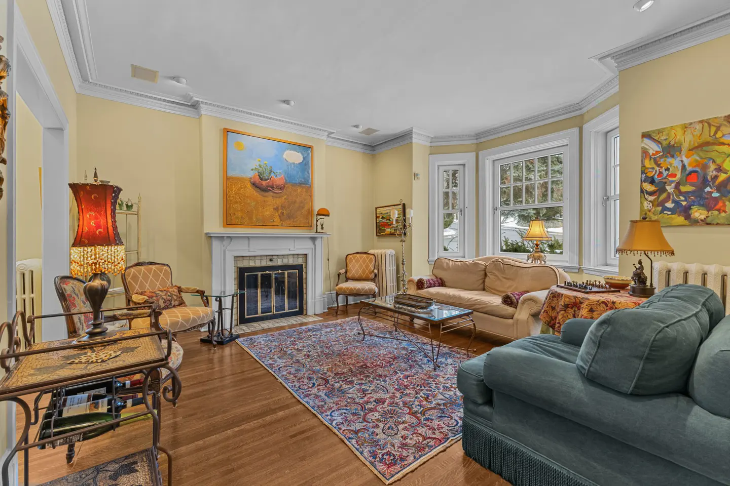 Living room with yellow walls, hardwood floors, and a fireplace. A blue rug sits in the center, with sofas and chairs around the room.