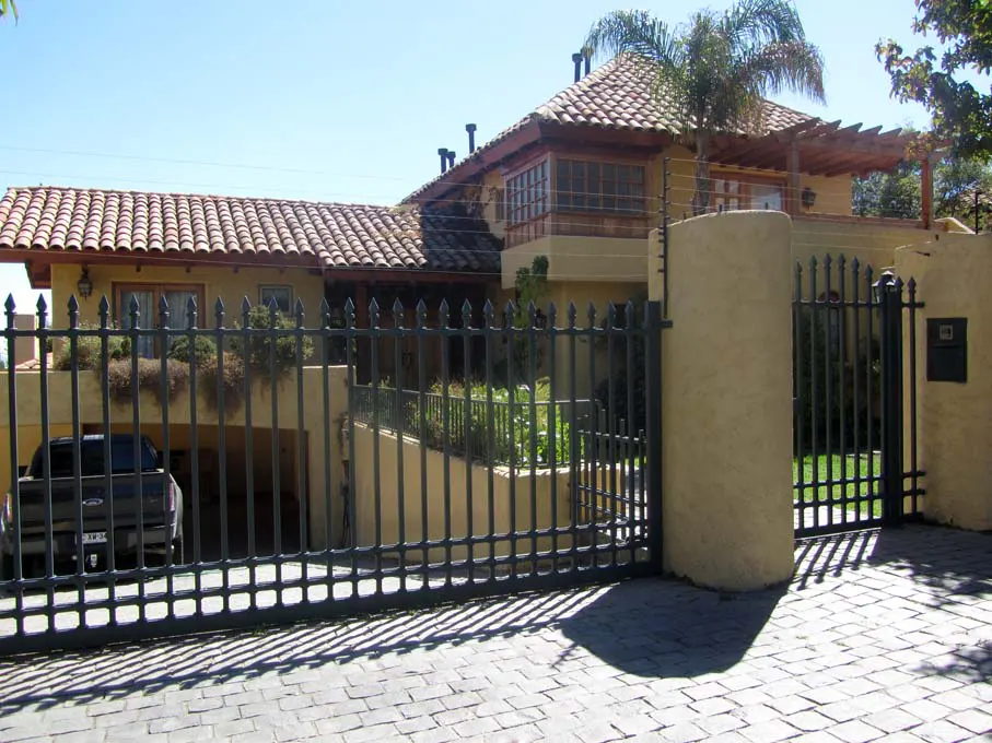 A tan two-story house with a red tile roof is behind a black iron gate. A black truck is parked in the garage.
