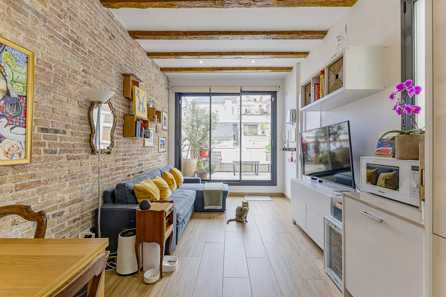 Living room with exposed brick wall, blue sofa with yellow pillows, wood floors, and a cat sitting in the center.