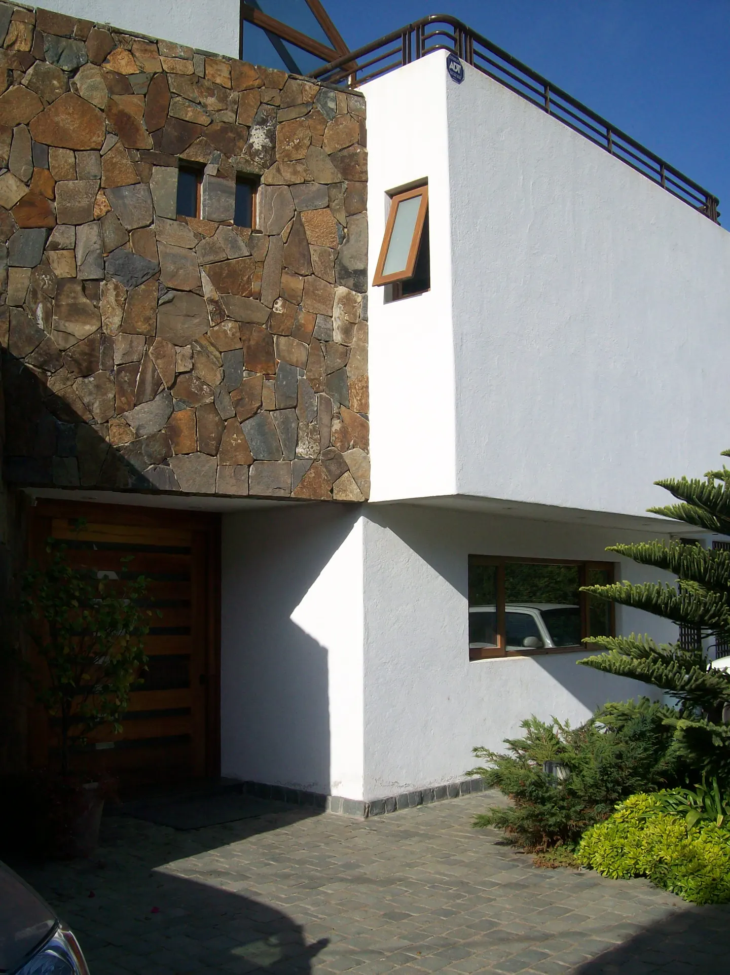Modern home exterior with stone accent wall, white stucco, wood garage door, and manicured landscaping.
