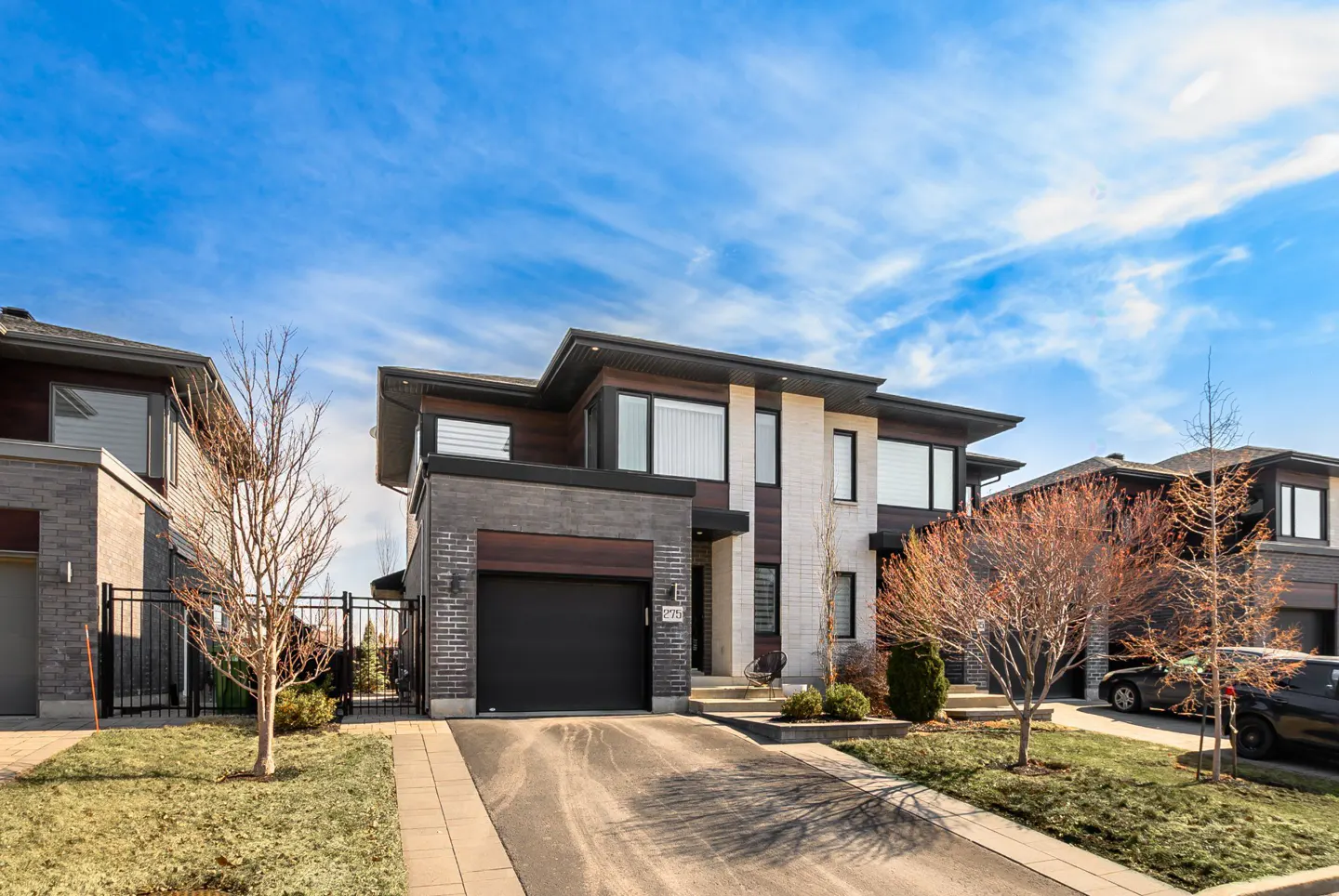Modern two-story house with a black garage door, brick and white stone facade, and a paved driveway under a blue sky.