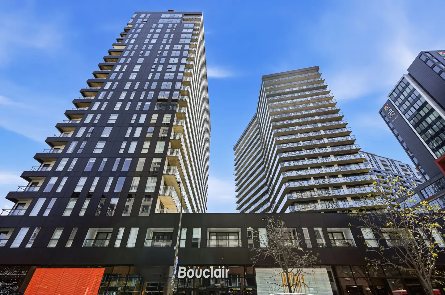 View of modern high-rise buildings with balconies and large windows against a blue sky. "Bouclair" storefront is visible.