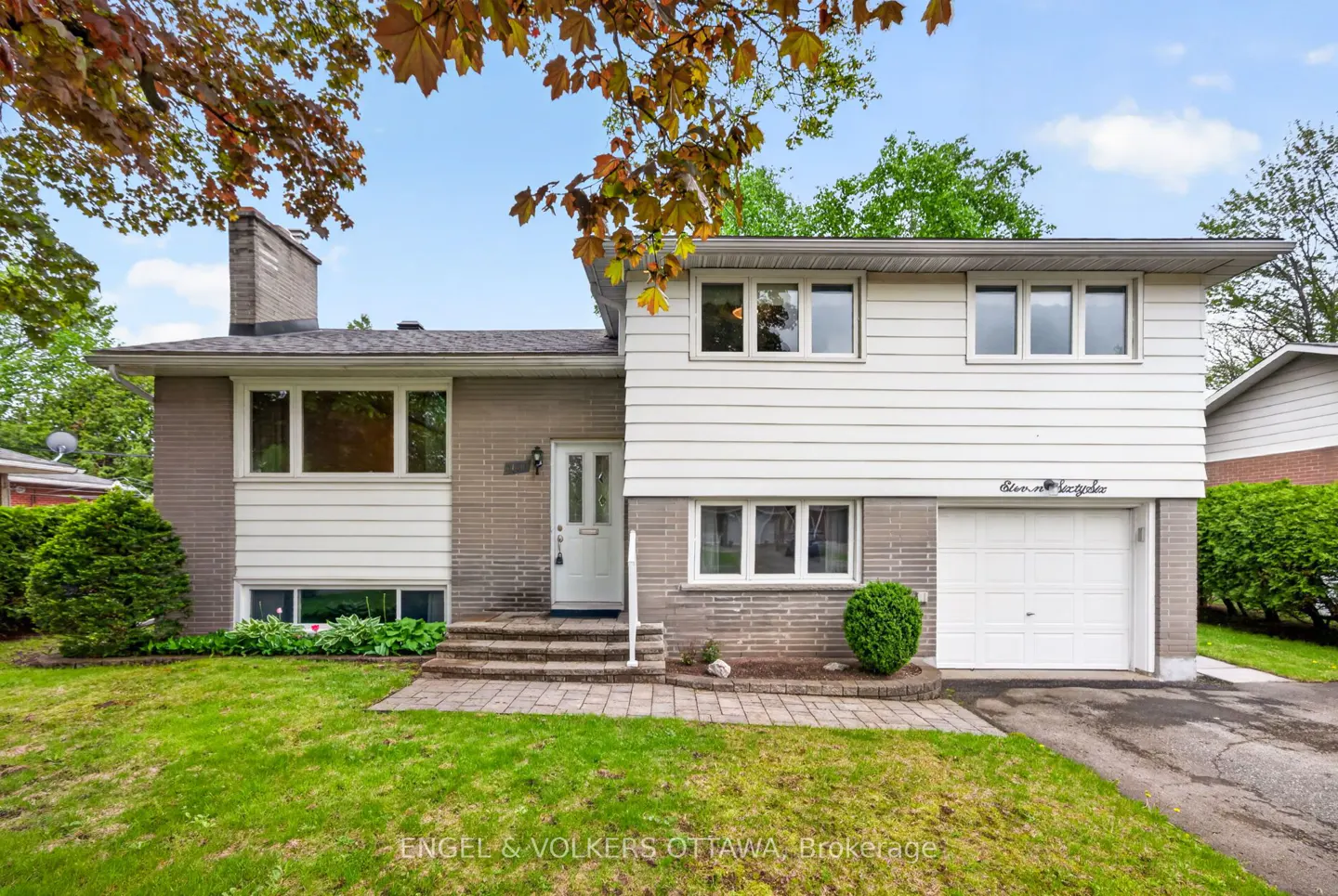 Two-story house with gray brick and white siding, a white garage door, and a green lawn.