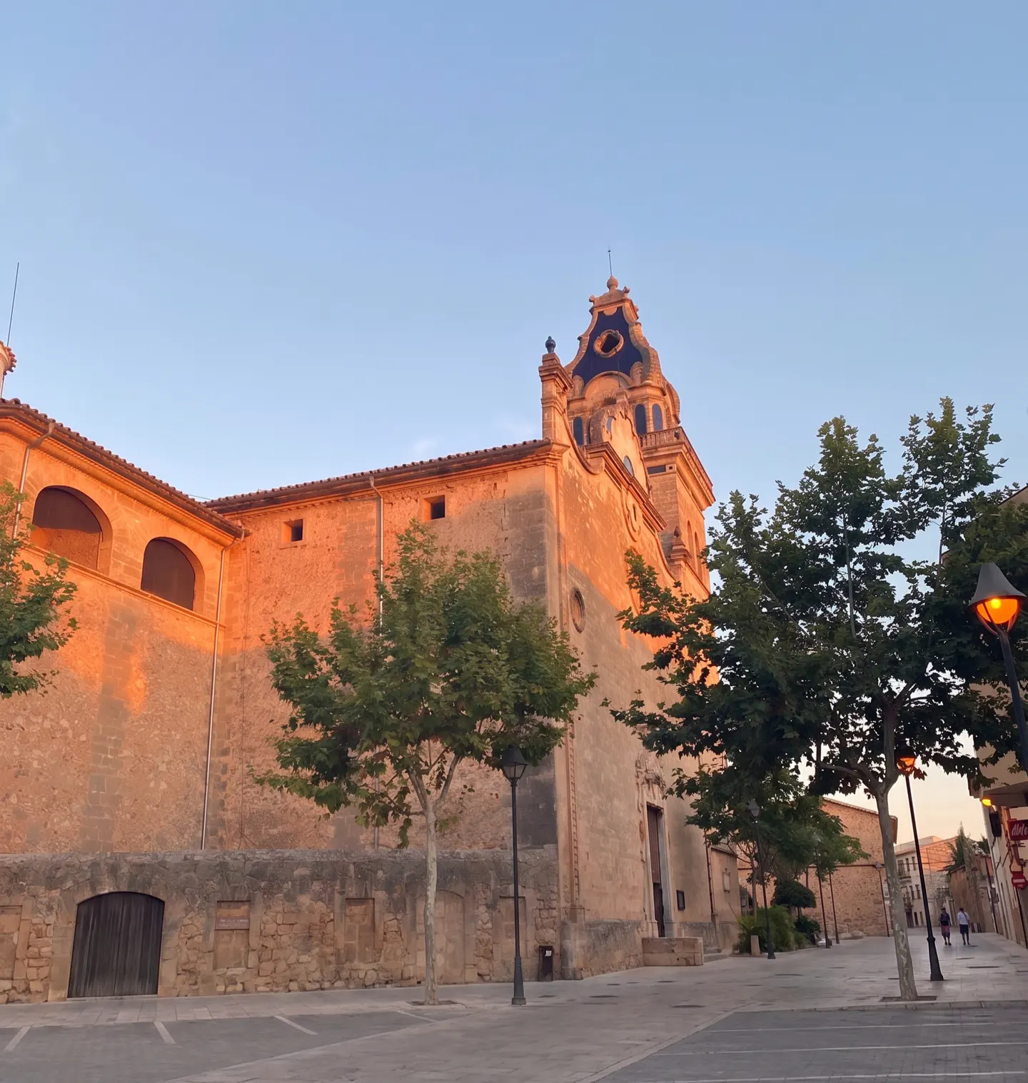 Stone church with blue dome at sunset. Trees line the street, and a lamppost glows orange.