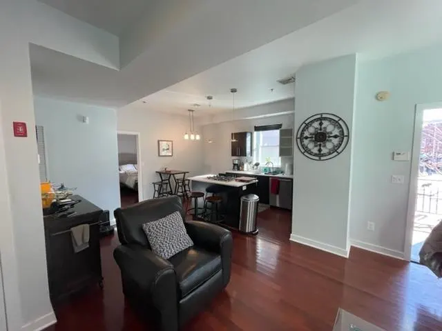 A living room with a black leather chair, wood floors, and an open kitchen with an island.
