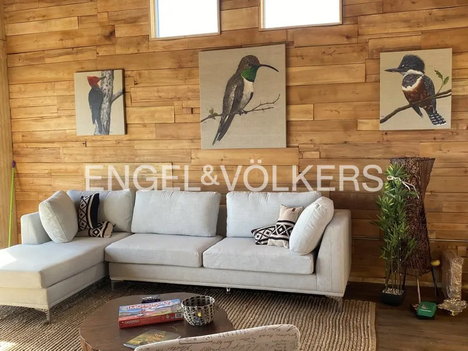 Living room with wood paneled walls, bird art, and a light gray sectional sofa. Engel & Völkers logo is visible.