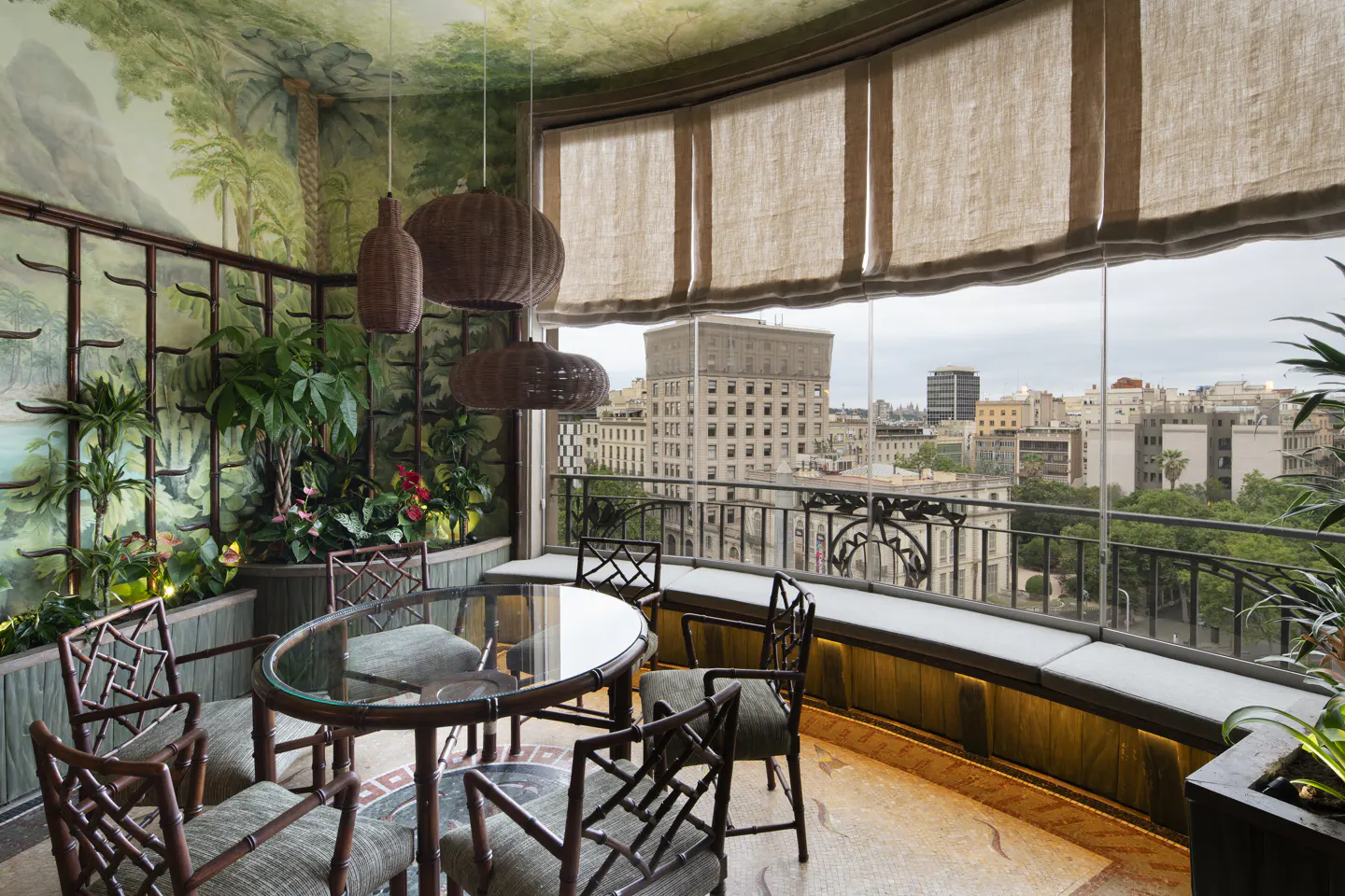 Sunroom with bamboo-style chairs, glass table, tropical mural, and large windows overlooking a city skyline.