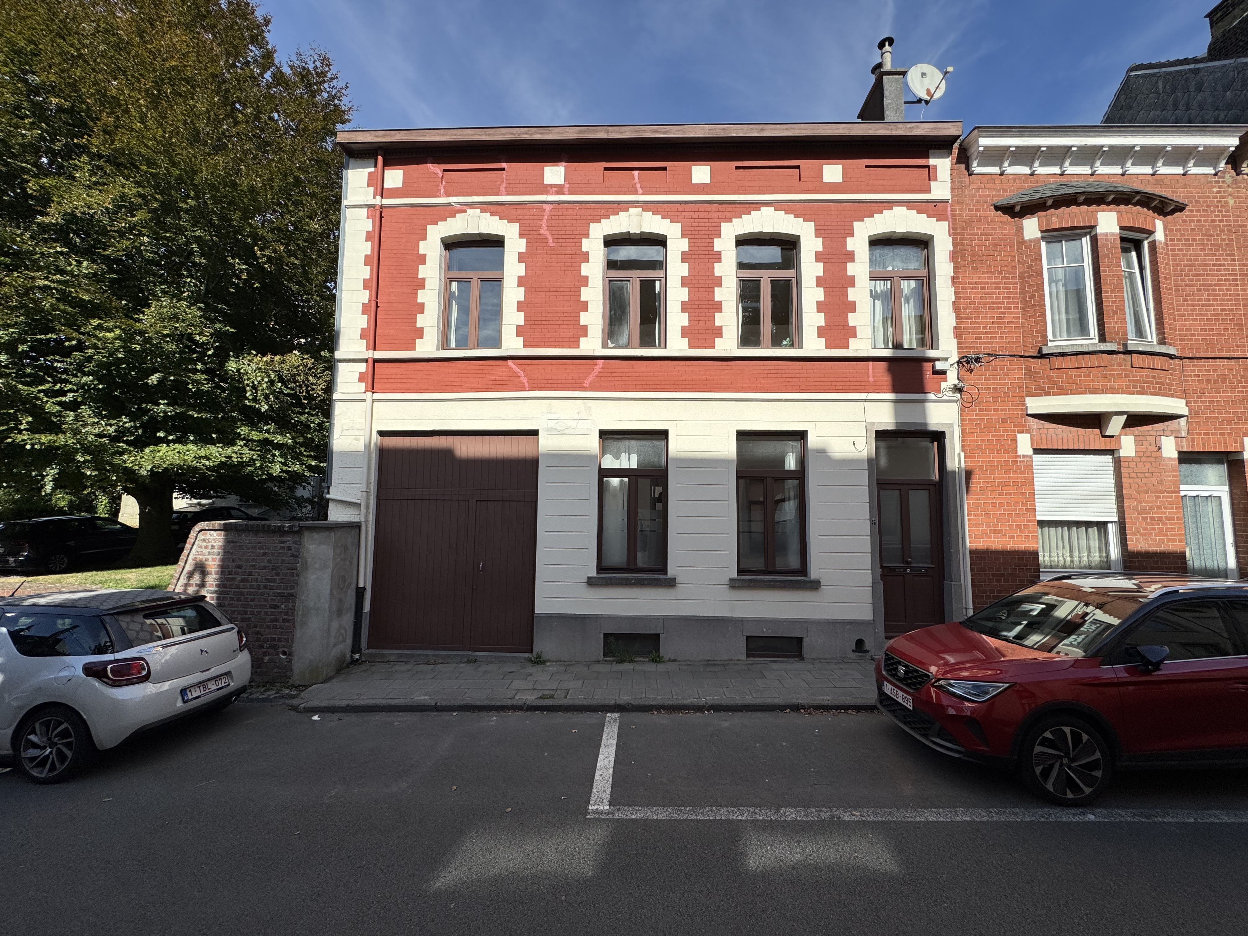 Two-story brick house with a red upper level, white lower level, large garage door, and cars parked on the street. [AI-generated text]